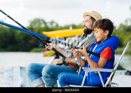 Padre e figlio tenendo la pesca affronta mentre la pesca insieme Foto Stock