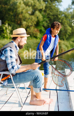 Dai capelli scuri boy rete di contenimento mentre la pesca con il padre Foto Stock