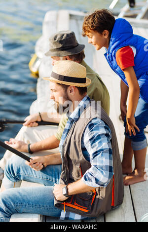Ragazzo curioso la visione di suo padre e suo nonno la pesca Foto Stock