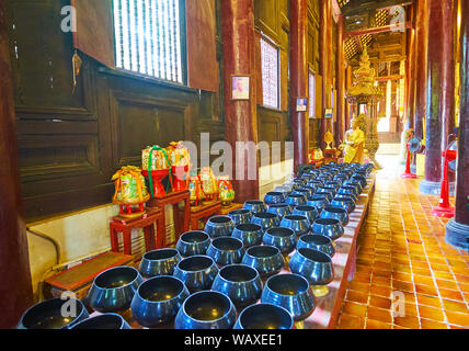 CHIANG MAI, Thailandia - 2 Maggio 2019: la lunga fila di donazione bocce nella parte anteriore del golden immagine del Buddha in teak medievale viharn (preghiera hall) di Wat Phan T Foto Stock