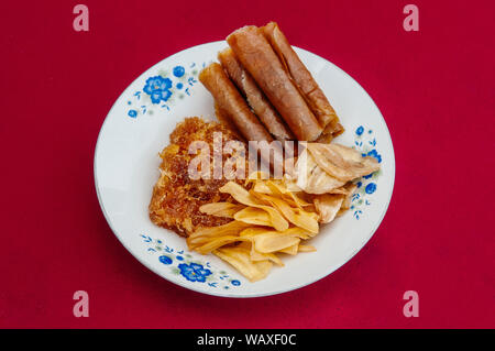 Tailandese locale fatta di frutta secca snack dolce - Foglio di Mango, banana Croccanti patatine e conserve pinsapple inceppamento spessa sul piatto con sfondo rosso Foto Stock