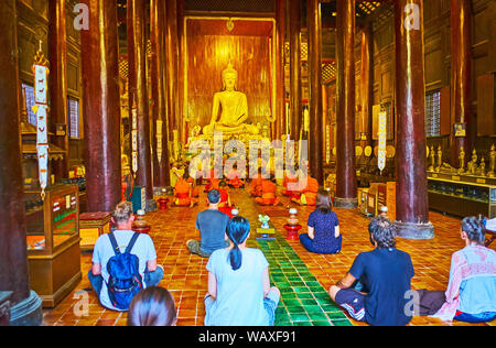 CHIANG MAI, Thailandia - 2 Maggio 2019: il culto in teak medievale Wat Phan Tao tempio; bhikkhu monaci sedersi davanti all altare e buddista devoto Foto Stock