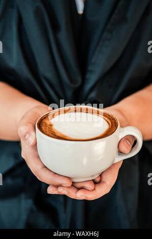 Mani femminili coppa di ritegno di bellissimi caffè caldo cappuccino con una bella forma di latte sulla parte superiore, vicino up shot Foto Stock