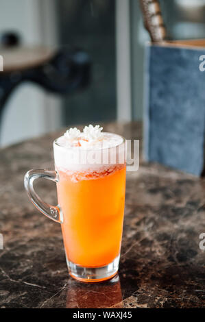 Un bicchiere di tè al gelsomino orange cocktail di birra con il soffice schiuma bianca tailandese e fiori di gelsomino sulla parte superiore Foto Stock