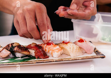 Chef asiatico mettere la cipolla tagliata a fettine su molti tipi di sushi giapponese su piastra in ceramica, Otoro, gamberi,carni bovine,il foie gras. Foto Stock