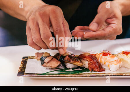 Chef asiatico mettere la cipolla tagliata a fettine su molti tipi di sushi giapponese su piastra in ceramica, Otoro, gamberi,carni bovine,il foie gras. Foto Stock