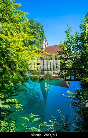 Blaubeuren, Germania, 29 giugno 2019, la celebre chiesa edificio di Blaubeuren abbey e molte persone si riflette nel vitreo acqua cristallina del vaso blu (B Foto Stock