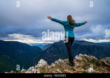 Montenegro, bella giovane donna con le braccia tese ampia permanente al bordo della spettacolare fiume Tara canyon nel Parco Nazionale del Durmitor natura terre Foto Stock