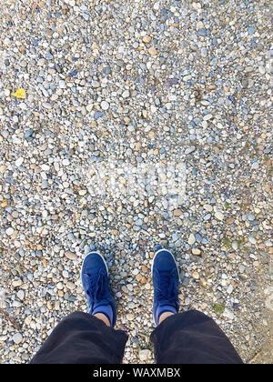 Guardare in basso al blue sneakers sulla ghiaia. Un uomo in pantaloncini casual e blu sneakers. Foto Stock