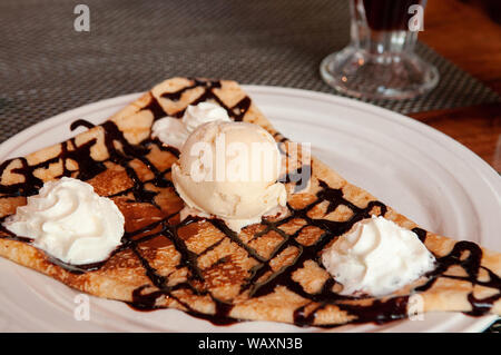 Il francese pasticceria semplice caldo crêpe con il freddo di gelato alla vaniglia e panna montata su piastra bianca - close up Foto Stock