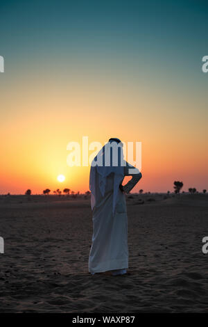 Uomo arabo sta solo nel deserto e guardare il tramonto Foto Stock