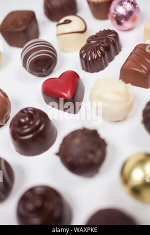 Cioccolatini fatti a mano o di caramelle tra cui un romantico a forma di cuore ad uno rosso fotografato dal di sopra su sfondo bianco Foto Stock