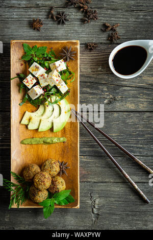 Il tofu e i falafel con verdure fresche, avocado e spezie su una piastra e tavolo in legno, vista da sopra, lo stile orientale Foto Stock