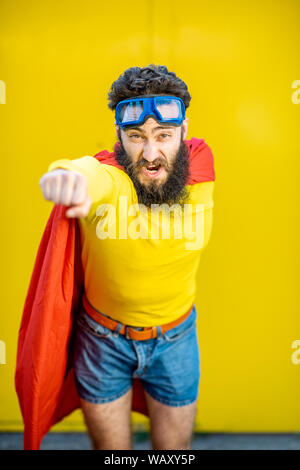 Ritratto di un uomo come un supereroe in abiti colorati e pilota gli occhiali su sfondo giallo Foto Stock