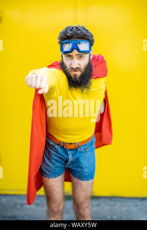 Ritratto di un uomo come un supereroe in abiti colorati e pilota gli occhiali su sfondo giallo Foto Stock