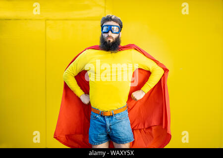 Ritratto di un uomo come un supereroe in abiti colorati e pilota gli occhiali su sfondo giallo Foto Stock