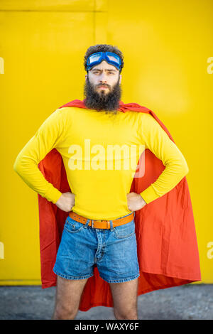 Ritratto di un uomo come un supereroe in abiti colorati e pilota gli occhiali su sfondo giallo Foto Stock