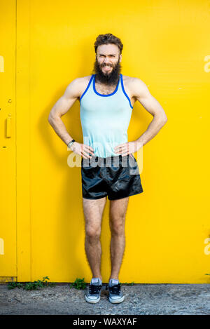 Ritratto di un energico, vecchio atleta vestito in 80s style esercitando su sfondo giallo Foto Stock