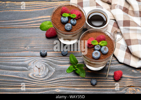 Tiramisù classico dessert con mirtilli e fragole in un bicchiere di vetro su sfondo di legno Foto Stock