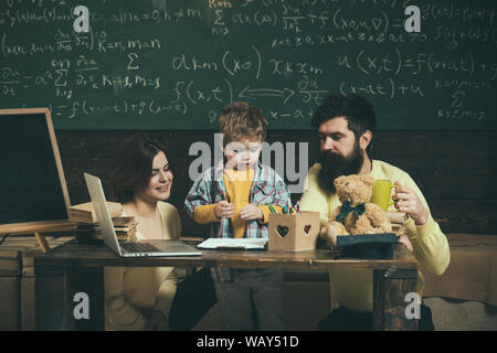 I genitori insegna figlio, lavagna su sfondo. Ragazzo ascolto di mamma e papà con attenzione. La famiglia si preoccupa di educazione dei loro figlio. Homeschooling c Foto Stock