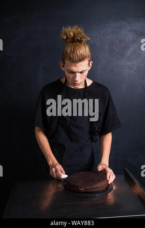 Il giovane chef con curva di taglio di capelli la torta in due pezzi Foto Stock