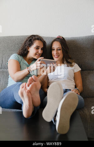 Ragazze in un lettino con i piedi in una tabella alla ricerca di un telefono cellulare Foto Stock