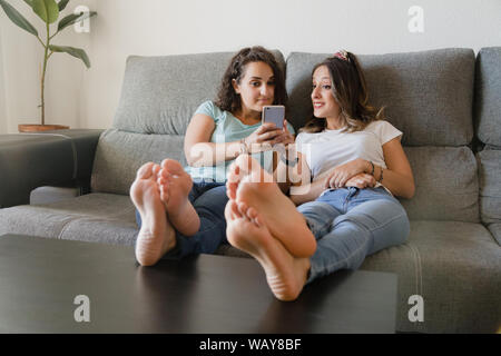 Due ragazze in un lettino con i piedi in una tabella con un telefono  cellulare Foto stock - Alamy