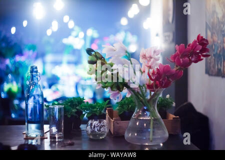 Profumo di rosa phalaenopsis orchidee in vaso di vetro, una bottiglia di acqua minerale e un bicchiere di acqua sul tavolo su uno sfondo sfocato di un negozio di fiori, sele Foto Stock