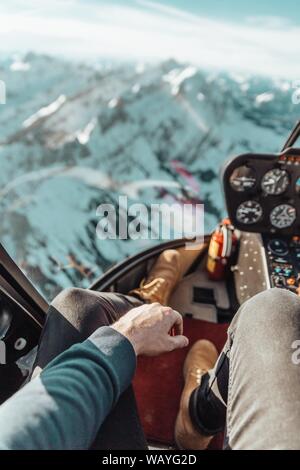 colpo di un maschio che indossa scarpe marroni e pantaloni grigi all'interno di un elicottero sopra le montagne Foto Stock