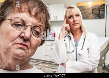 Di empatico medico in piedi dietro turbato Senior donna adulta in ufficio. Foto Stock