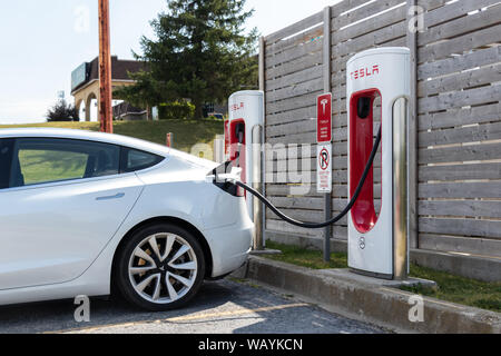 Bianco modello Tesla 3 visto inserito in Tesla Supercharger stazione. Foto Stock