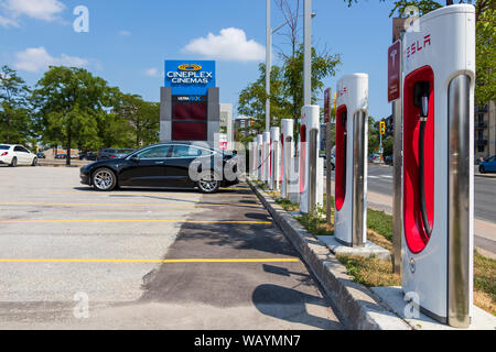 Tesla Modello 3 in sosta e la carica a Tesla Supercharger stazione sulla giornata di sole. Foto Stock