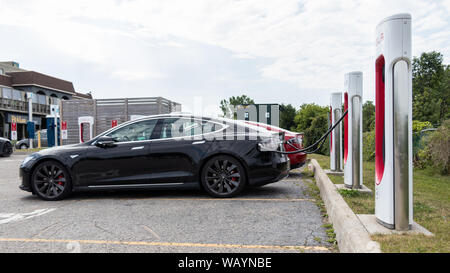 Nero modello Tesla S collegata a una presa di corrente e la carica a Tesla Supercharger Station con altri veicoli in carica dietro. Foto Stock