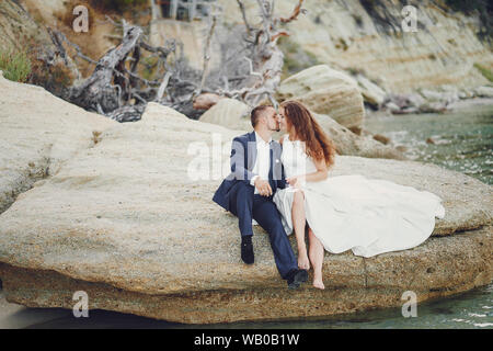 Giovane e bella con i capelli lunghi sposa in abito bianco con il suo giovane marito vicino al fiume Foto Stock