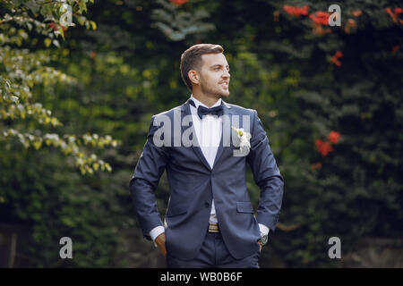 Una bella ed elegante sposa in una tuta blu sorge in un parco estivo vicino le boccole con bouquet Foto Stock