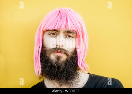 Close-up verticale di un uomo elegante con la barba e lunghi capelli a colori su sfondo giallo Foto Stock