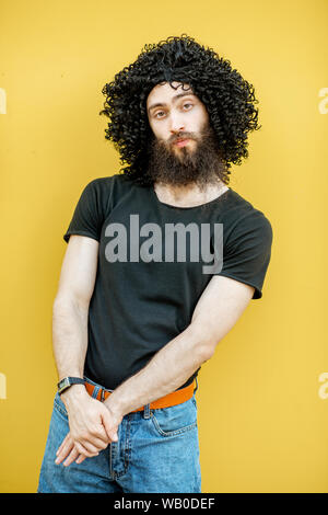 Ritratto di uno strano uomo con curley capelli neri in piedi su sfondo giallo Foto Stock
