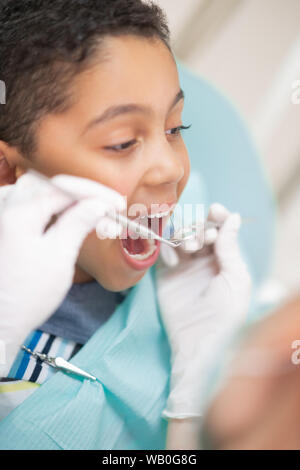 Bello dai capelli scuri boy bocca di apertura mentre la visita dal dentista Foto Stock