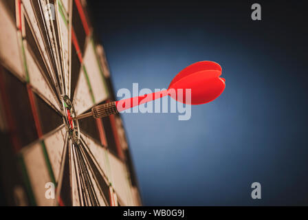 Dart rosso al centro di un bersaglio o a freccette punteggio scheda di un occhio di bue in una immagine concettuale su blu con spazio di copia Foto Stock