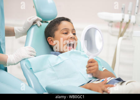 Ragazzo bocca di apertura e guardando nel retrovisore durante la visita dal dentista Foto Stock