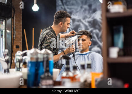 Close-up, master barbiere fa la pettinatura e lo styling con essiccatore, asciuga i capelli a guy. Concetto Barbiere. Soft focus. Foto Stock