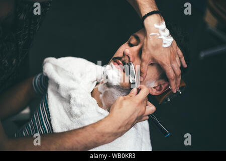 Rasoio in mani di specialista barbiere. Rasatura barbiere un uomo in un barbiere, close-up. L'uomo mith mustaches avente una rasatura Foto Stock