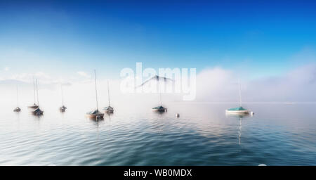 Nebbia sul Lago di Thun con barche a boe di ancoraggio e montagna Niesen sporgenti nel cielo blu Foto Stock