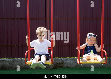 Davvero godere di essa. Ragazzo e una ragazza gli stili di taglio di capelli. Parrucchiere per bambini. Bambini piccoli con capelli biondi sull'altalena. Piccolo fratello e sorella di godere il gioco Foto Stock