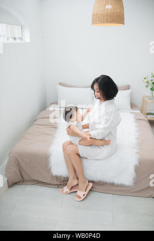 La famiglia felice. Il bambino e la madre figlia gioca, avvolgente, kissing a casa sul letto Foto Stock