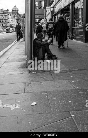 Glasgow, Scotland, Regno Unito - 22 Giugno 2019: le persone camminare davanti a un gentiluomo maschio ubicazione sul pavimento sporco con un McDonald's bicchiere di carta attraente per mon Foto Stock