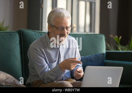 Felice vecchio uomo senior di ridere guardando rivolto verso lo schermo del notebook Foto Stock