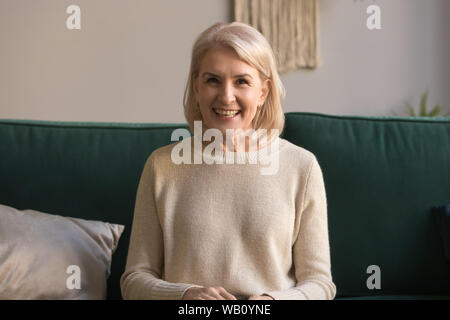 Sorridente donna di mezza età di parlare alla telecamera sedersi sul lettino Foto Stock