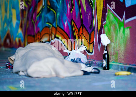 Mannheim, Germania. 23 Ago, 2019. Avvolto in un soffitto, una persona senzatetto dorme in un passaggio ponte su una parete dipinta con graffiti. Credito: Uwe Anspach/dpa/Alamy Live News Foto Stock