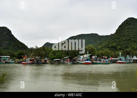 Barche da pesca galleggiante nelle acque presso il villaggio di pescatori del porto con la montagna in background a divieto Bangpu, Khao Sam Roi Yot, Thailandia Foto Stock